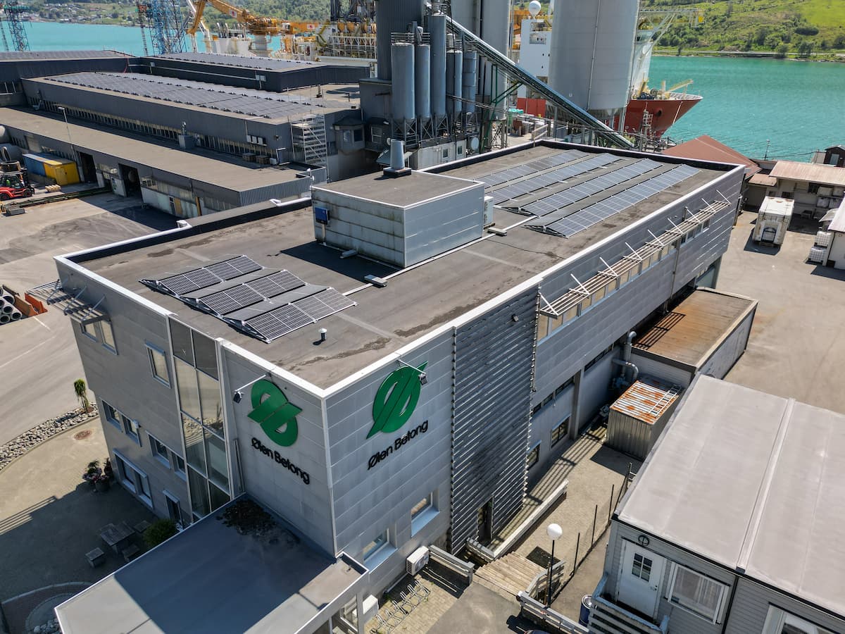 Dronebilde av administrasjonsbygget i Ølensvåg og fabrikken i bakgrunnen, begge med nye solcelleanlegg på taket.