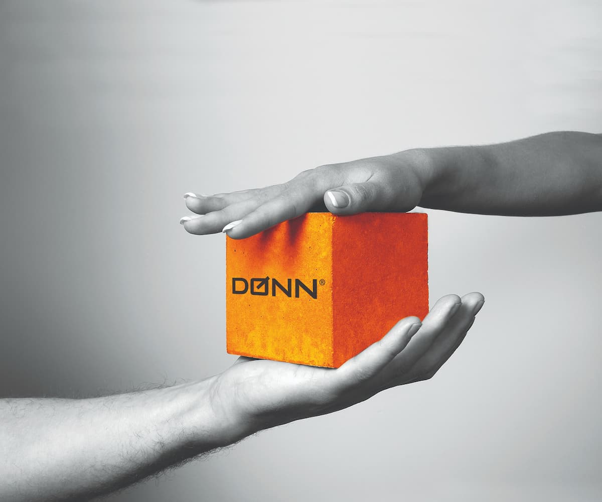 En oransje betongkloss med Dønn-logo mellom 2 hender